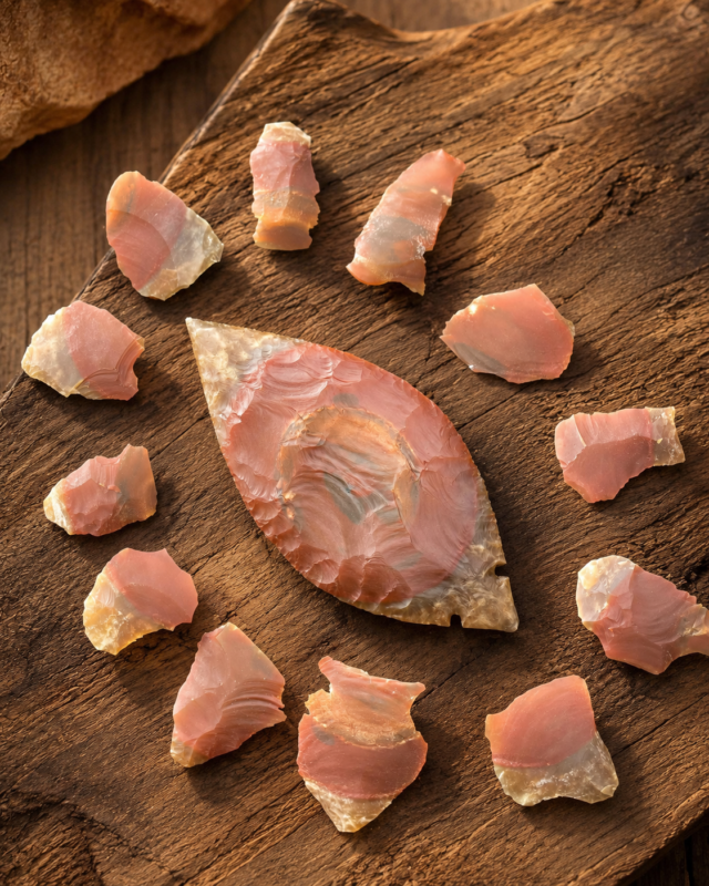 Handcrafted Fulton Turkey Tail point flintknapped from Kentucky Carter Cave Chert, displaying natural pink banding and surrounded by flakes of the original stone by Joel Robinson.