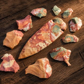Handcrafted Dovetail point flintknapped from colorful Flint Ridge Flint, displaying vibrant natural patterns and surrounded by flakes of the original stone by Joel Robinson.