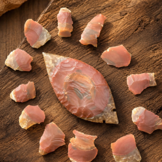 Handcrafted Fulton Turkey Tail point flintknapped from Kentucky Carter Cave Chert, displaying natural pink banding and surrounded by flakes of the original stone by Joel Robinson.